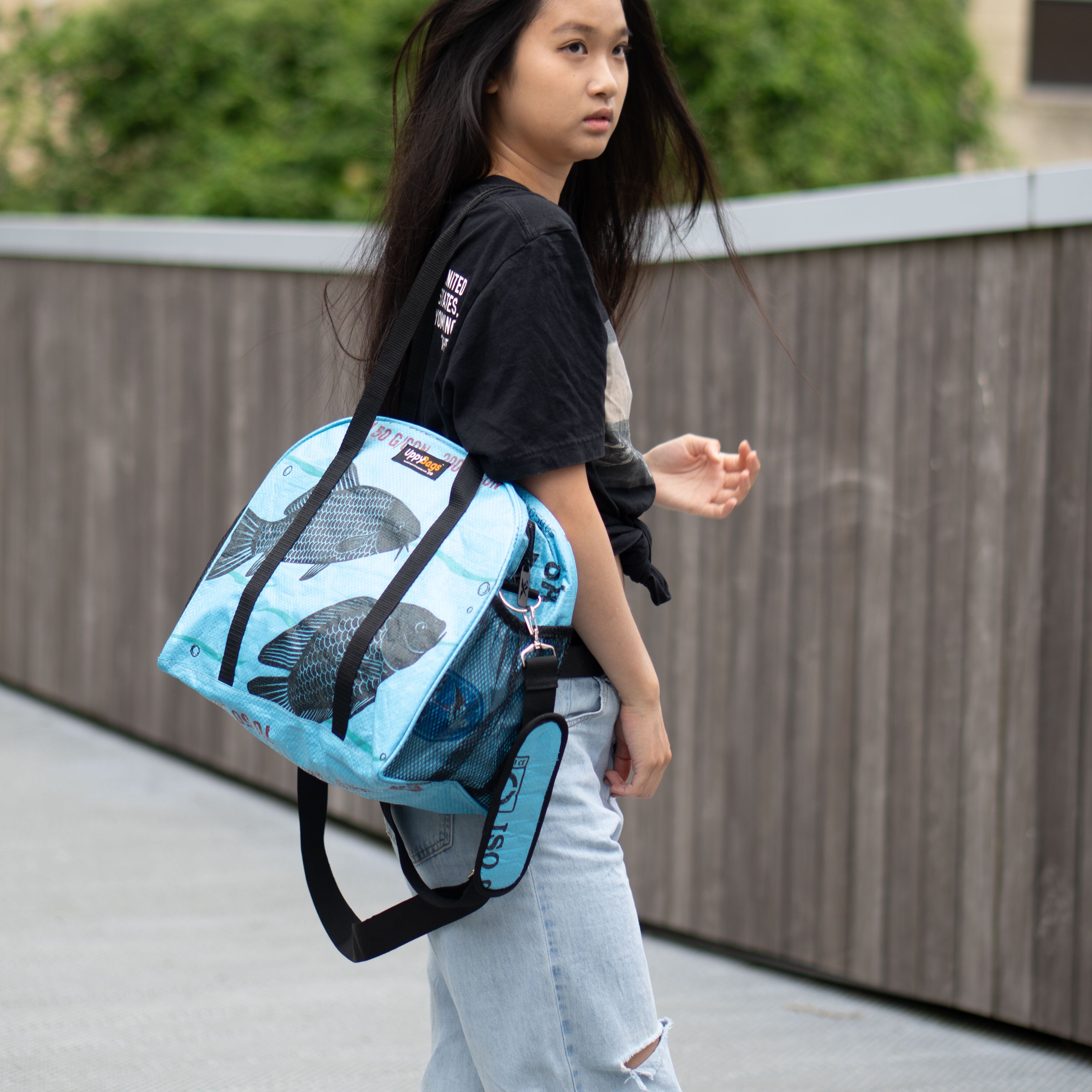 Person wearing a blue shoulder bag with a visible brand logo on a wooden pathway.